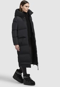 Melna garā pilda mētelis ar augstu apkakli, ar rāvējslēdzēja priekšpusi, sānu kabatām un elegantu dizainu. Apvienots ar melnām izolētām zābakiem.