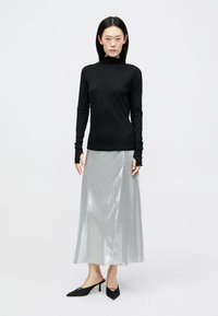 Črna dolga majica s turtleneck ovratnikom in rebrasto teksturo, v kombinaciji s sijočo srebrno krilo do gležnjev in črnimi čevlji s koničastim nosom.