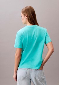 Maglietta di cotone turchese con maniche corte, vestibilità comoda e scollo tondo. Il tessuto appare morbido e liscio, senza motivi visibili.