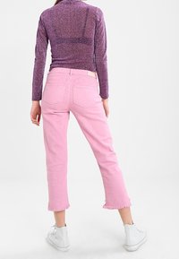 Jeans cortos rosas con dobladillos deshilachados, combinados con una blusa ligera de manga larga en tono púrpura que presenta una sutil textura brillante.