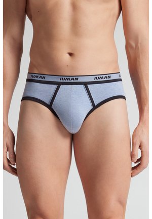 Pánský trup oblečený v světle modrých slipkách s černým lemováním a pasem označeným nápisem "IUMAN" na jednobarevném šedém pozadí.