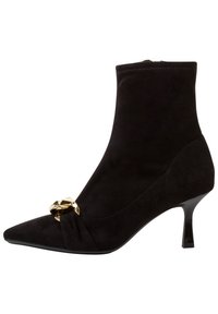 Bottine noire en cuir suédé avec bout pointu, présentant un design frontal torsadé et un accent en chaîne dorée. Un talon haut mince complète le look.