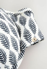 Aluspesu, millel on valge põhivärv ja tumesinised sõnajalalehed, sile tekstuur ning kuldse tooniga detail bändil.