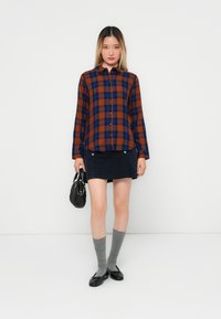 Brown and blue plaid button-up shirt, black corduroy skirt, gray knee-high socks, black flats, and a small black handbag.