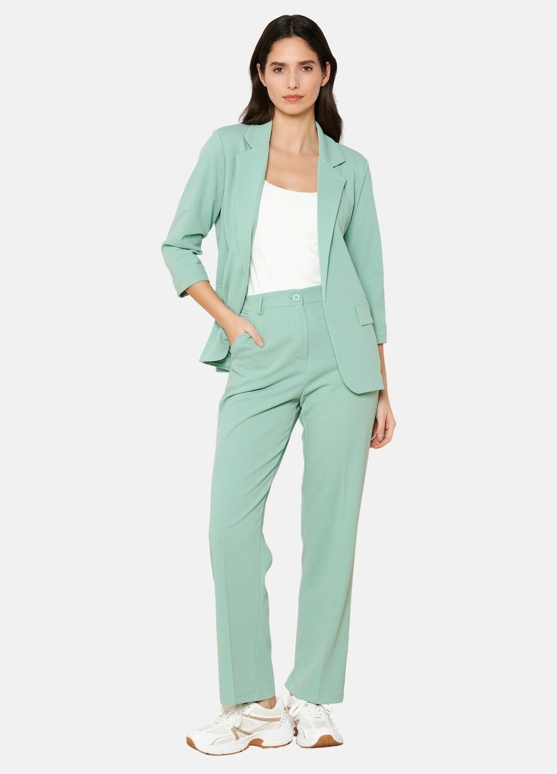 Svetlo zelena blazer in ujemajoče hlače iz gladkega materiala. Oblačilo vključuje belo majico in bele superge z svetlobnimi rjavimi poudarki.
