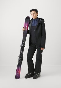 Schwarze Skijacke und -hosen mit einer blauen Innenschicht, die lila und schwarze Skier mit Bindungen hält. Schlankes, modernes Design, geeignet für Wintersport.