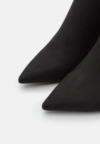 Svarta mocka pumps med spetsig tå och en slät textur, med en elegant silhuett och smal design.