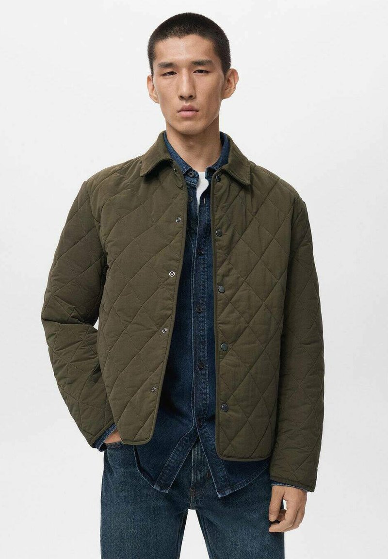 Olijfgroene gewatteerde jas met een ruitpatroon, drukknopen en een kraag. Gdragen over een blauwe denim shirt.