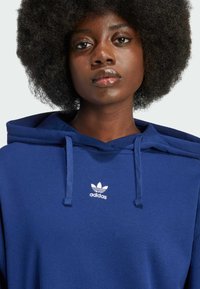 Mörkblå luvtröja i mjuk bomull; har en justerbar dragsko i luvan och en vit Adidas-logotyp på bröstet, med en ledig passform.