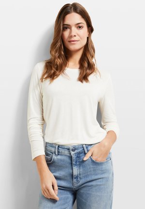 Hellbeige Langarmshirt mit runder Ausschnitt, kombiniert mit hellblauen Jeans. Der Stoff wirkt weich mit einer glatten Textur.
