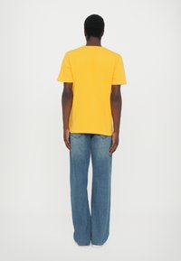Tricou galben din bumbac, cu mâneci scurte, guler rotund, asortat cu blugi largi de culoare albastru deschis. Design simplu, fără modele sau logo-uri vizibile.