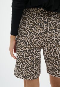 Shorts en imprimé léopard en tissu texturé, dotés de poches arrière et d'un ourlet retroussé. Le design incorpore des tons marron terreux et des nuances de rose.