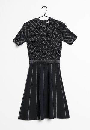 Vestido negro de manga corta con patrón de diamantes en la parte superior y rayas verticales en la falda acampanada, colgado en una percha negra sobre fondo blanco.