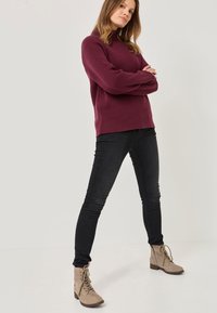 Maglione a maglia bordeaux con texture a coste, abbinato a jeans skinny neri e stivaletti color cammello con lacci e tacco basso.