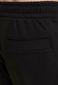 Black sweatpants featuring a stretchy waistband and a small, stitched pocket detail, made from soft, smooth fabric.