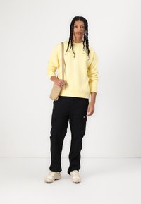 Yellow sweatshirt with ribbed cuffs, black cargo pants with side pockets, and beige crossbody bag; model wearing cream-colored sneakers.