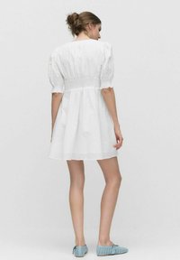 Robe blanche courte avec des manches bouffantes, taille cintrée et jupe évasée. Tissu texturé. Portée avec des chaussures perforées bleu clair.