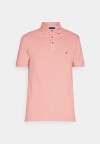 Rosa bomullspikétröja med treknappskrage, korta ärmar och en liten logotyp på vänster bröst, slät textur.