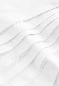 Biała tkanina z delikatnymi fałdami, gładką teksturą i subtelnymi detalami ściegów, tworzącymi miękkie, płynące linie na powierzchni.
