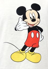 Hvid T-shirt med en tegneseriefigur med sorte ører, røde shorts og gule sko, vist i en venlig positur med tommelfinger-op gestus.