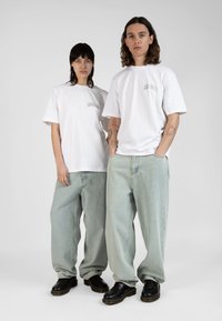 Uformell antrekk med hvite bomulls t-skjorter med logo foran, lyseblå baggy-jeans og sorte snøresko med teksturert såle.