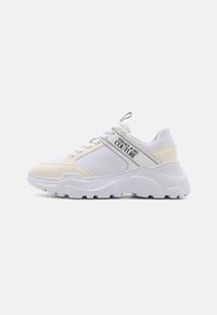 Sneaker bianca con una combinazione di tessuto morbido e dettagli in suede, una suola chunky e un logo ben visibile sul lato.