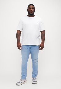 Hvit bomull T-skjorte, rund hals, avslappet passform, sammen med lyseblå jeans og grå joggesko med hvite detaljer.