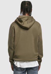 Oliwkowa zielona bluza z kapturem o miękkiej fakturze, wyposażona w kaptur ze sznurkiem i ściągacze na rękawach. Pod spodem widoczna warstwowa biała koszula.