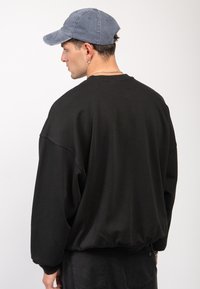 Črn oversize pulover s spušenimi rameni, z rebrastim robom, izdelan iz bombaža. Uporabljen z modro kapo in vsebuje srebrno uho.