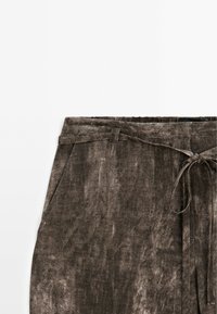 Pantalon en velours marron avec poches latérales et une fine ceinture en tissu nouée en nœud à la taille.