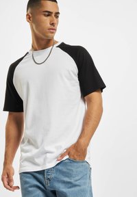 Herrtröja i baseballstil med korta svarta ärmar och vit kropp. Tillverkad av mjukt tyg, med rund halsringning och avslappnad passform.