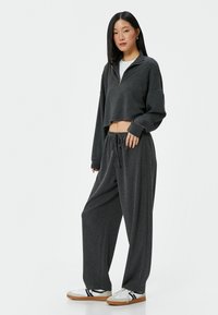 Grijze cropped zip-up sweatshirt en bijpassende wijdvallende pantalon. De stof lijkt textuur te hebben met een broek met een koord in de taille, gecombineerd met witte sneakers.