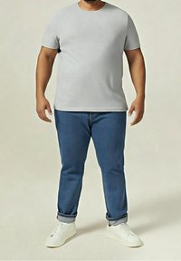 Šedé tričko s krátkým rukávem v kombinaci s modrými džínami. Tričko má kulatý výstřih, džíny jsou ohrnuté na nohavicích. Celý vzhled doplňují bílé tenisky.