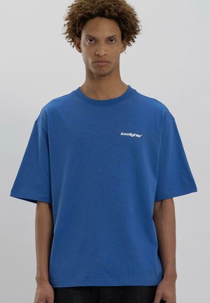 Blue cotton t-shirt with a relaxed fit and short sleeves, featuring a white logo on the chest. Smooth texture and crew neckline.