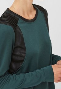 Zielona bluza z akcentami z czarnej ekoskóry, żebrowanym wzorem na ramionach i okrągłym dekoltem; miękka tekstura i dopasowane mankiety.