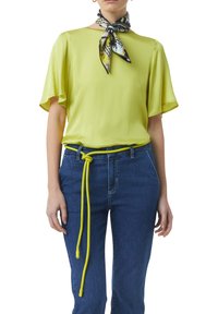 Light yellow short-sleeve blouse with a smooth texture, paired with blue denim jeans featuring a bright yellow knotted belt. Printed scarf accent.