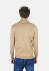Maglione beige lavorato a maglia con maniche lunghe e polsini a coste, visto da dietro. Abbinato a jeans blu con tasche posteriori.