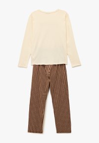 Langærmet cremefarvet top kombineret med brune ternede bukser. Toppen har en rund hals; bukserne har elastik i taljen og ternet mønster.