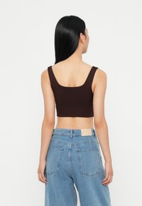 Brun cropped topp med brede skulderstropper, laget av stretchy stoff. Kombinert med lyseblå høytlivsjeans med baklommer.