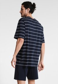 T-shirt rayé bleu marine avec des rayures horizontales blanches, fabriqué en tissu doux ; assorti avec un short bleu marine, à manches courtes et coupe décontractée.