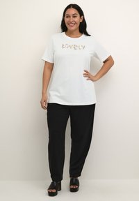 Hvid bomulds t-shirt med blomster "KÆRLIGHED" tekst, parret med sorte tapered bukser og sorte åbne platform-sko.