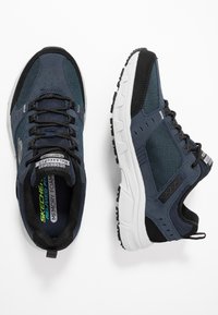 Męskie granatowe buty Skechers z górną częścią wykonaną z siateczki i zamszu. Charakteryzują się czarnymi akcentami, białą podeszwą środkową oraz teksturowaną podeszwą dla lepszej przyczepności. Wkładka z pianki pamięciowej.
