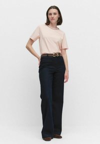 Ljust rosa kortärmad t-shirt med rund halsringning, kombinerad med mörkblå utsvängda jeans, samt brun bälte och bruna skor.