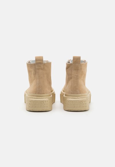 Beige suede ankle boots with a textured cream sole, featuring a back pull tab and minimalistic design, viewed from the rear.