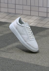 Weißer Sneaker mit Obermaterial aus glattem Leder, perforiertem Zehenbereich und Wildlederakzenten. Verfügt über eine flache weiße Sohle und tonale Schnürsenkel.