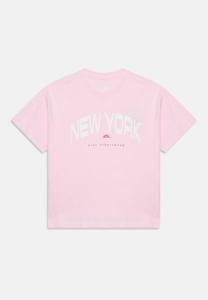 T-shirt Nike rose clair avec texte blanc "New York", logo rouge Nike et "Nike Sportswear" imprimé en dessous sur le devant.