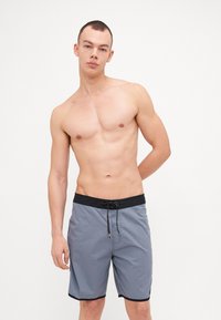 Pantaloni da bagno grigi con fascia in vita nera e cordoncino, caratterizzati da un design semplice e cuciture a contrasto. Materiale leggero e testurizzato.