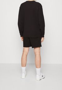 Svart långärmad skjorta med avslappnad passform, kombinerad med svarta shorts. Vita sneakers och strumpor fulländar outfiten. Minimalistisk design.