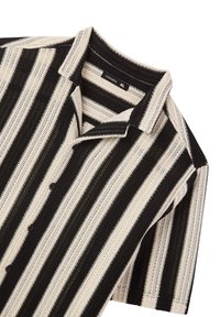 Camicetta a maniche corte a righe in nero e crema. Presenta una chiusura con bottoni frontale, colletto e un tessuto testurizzato con righe solide e aperte alternate.