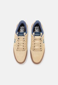 Beige velúr sportcipők sötétkék részletekkel, világosbarna orrfedővel, lapos fűzőkkel és perforált díszítésekkel az orrboxon. Etnies márkázás a nyelvén.